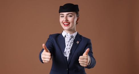 Photo of Charming stewardess showing thumbs ups on brown background