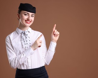 Photo of Beautiful stewardess pointing at something on brown background. Space for text