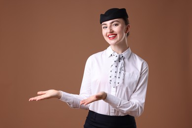 Photo of Beautiful stewardess showing something on brown background. Space for text