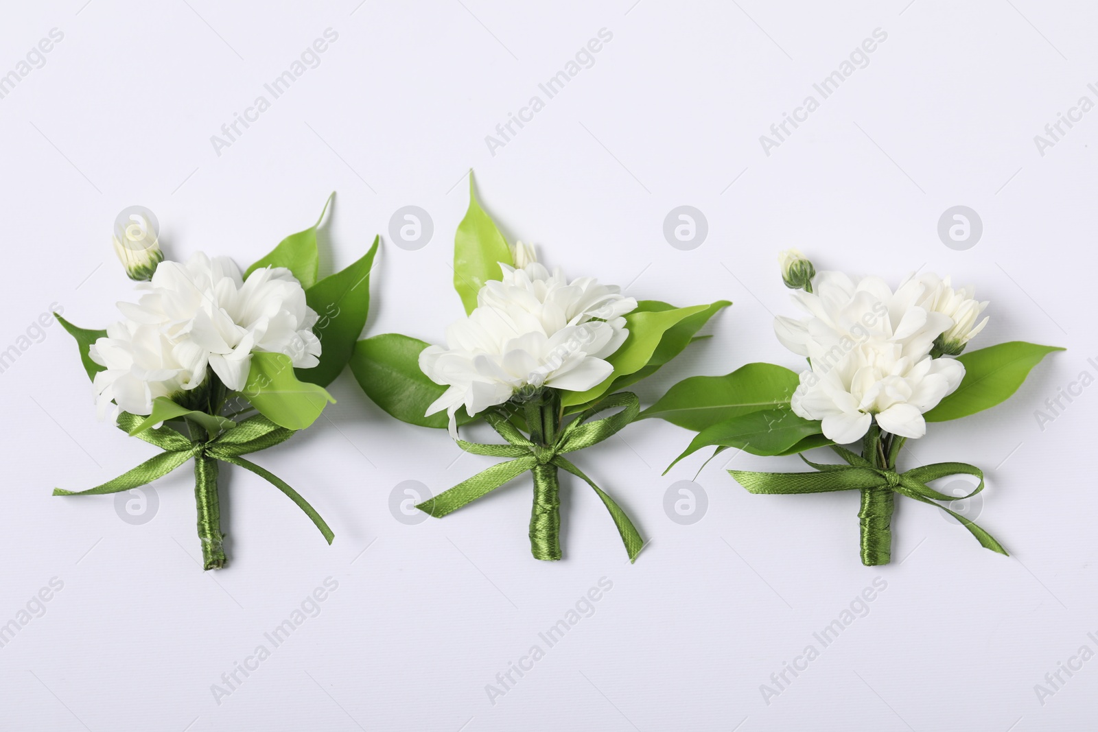 Photo of Boutonnieres with beautiful flowers on white background, flat lay