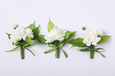 Photo of Boutonnieres with beautiful flowers on white background, flat lay