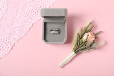 Photo of Beautiful boutonniere, wedding rings and lace fabric on light pink background, flat lay