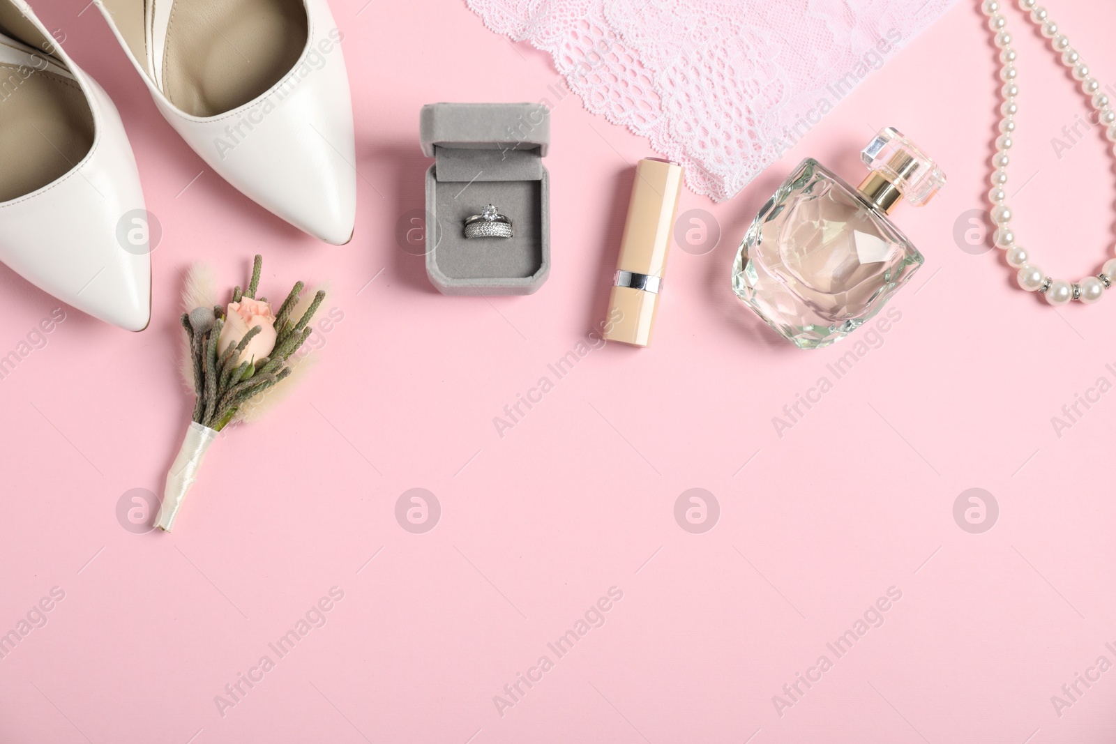 Photo of Flat lay composition with boutonniere, wedding rings and bride's accessories on light pink background. Space for text