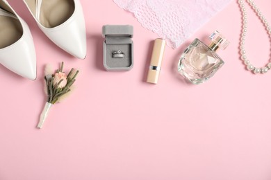 Photo of Flat lay composition with boutonniere, wedding rings and bride's accessories on light pink background. Space for text