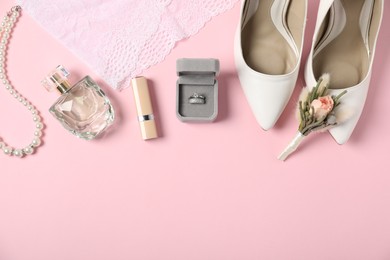 Photo of Flat lay composition with boutonniere, wedding rings and bride's accessories on light pink background. Space for text