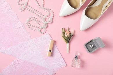 Photo of Flat lay composition with boutonniere, wedding rings and bride's accessories on light pink background