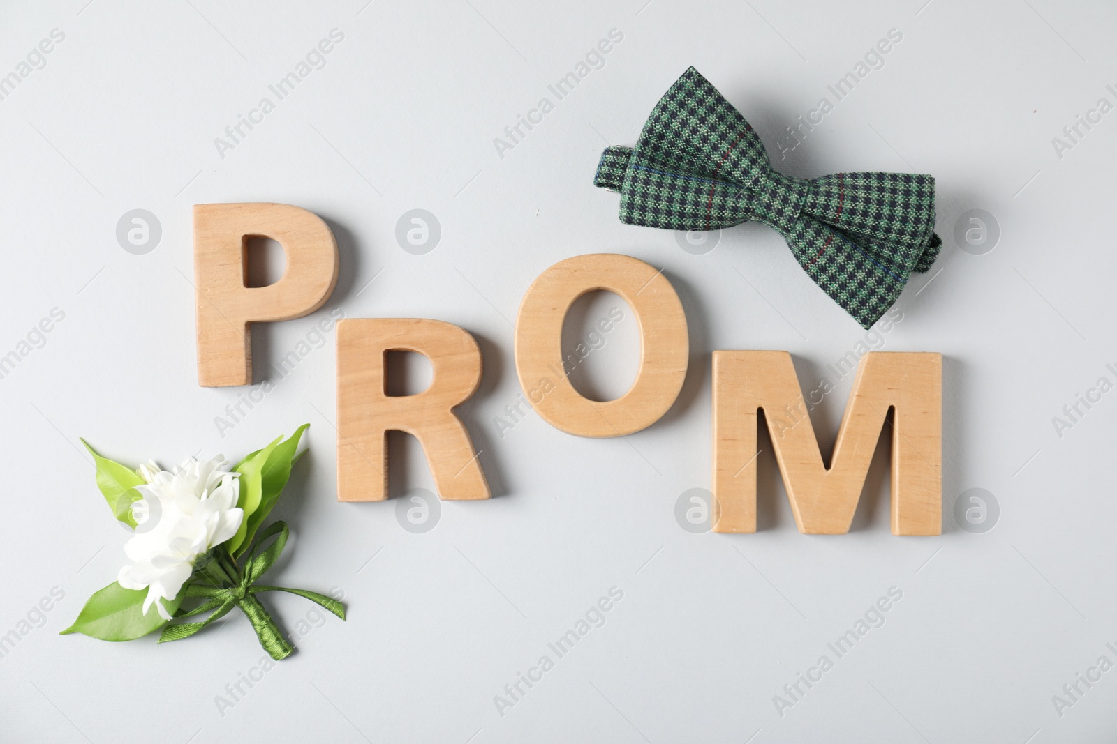 Photo of Word Prom made of wooden letters, boutonniere and bowtie on white background, flat lay