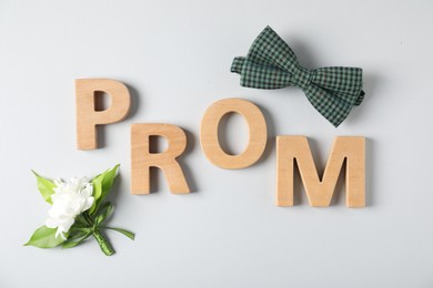 Photo of Word Prom made of wooden letters, boutonniere and bowtie on white background, flat lay