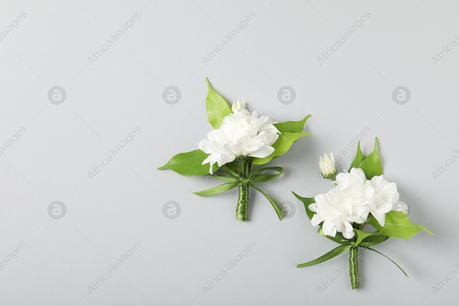Photo of Boutonnieres with beautiful flowers on light background, flat lay. Space for text