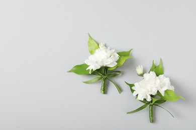 Photo of Boutonnieres with beautiful flowers on light background, flat lay. Space for text