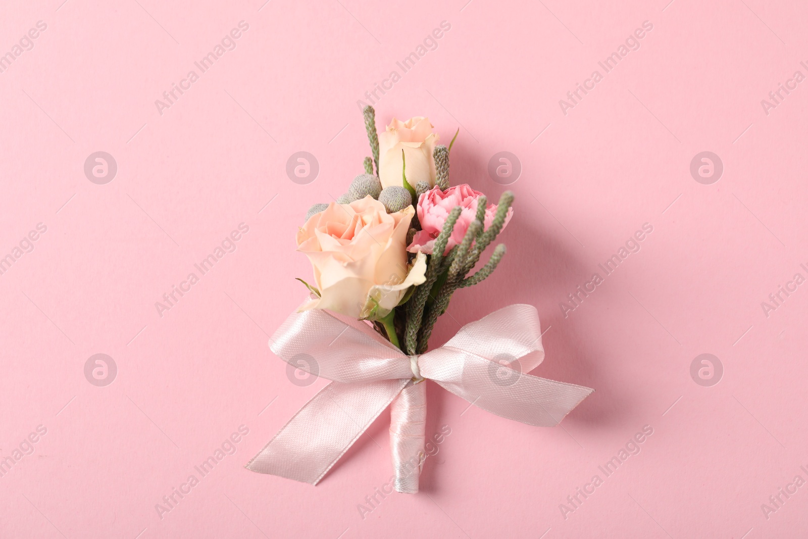 Photo of Boutonniere with beautiful flowers on light pink background, top view