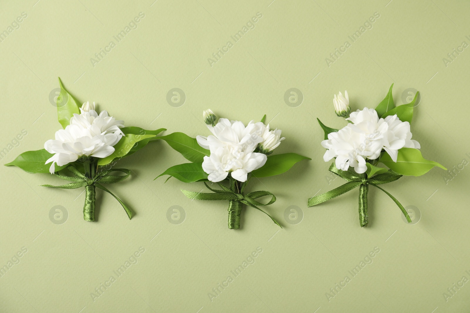 Photo of Boutonnieres with beautiful flowers on green background, flat lay