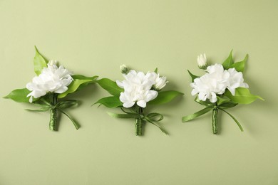 Photo of Boutonnieres with beautiful flowers on green background, flat lay