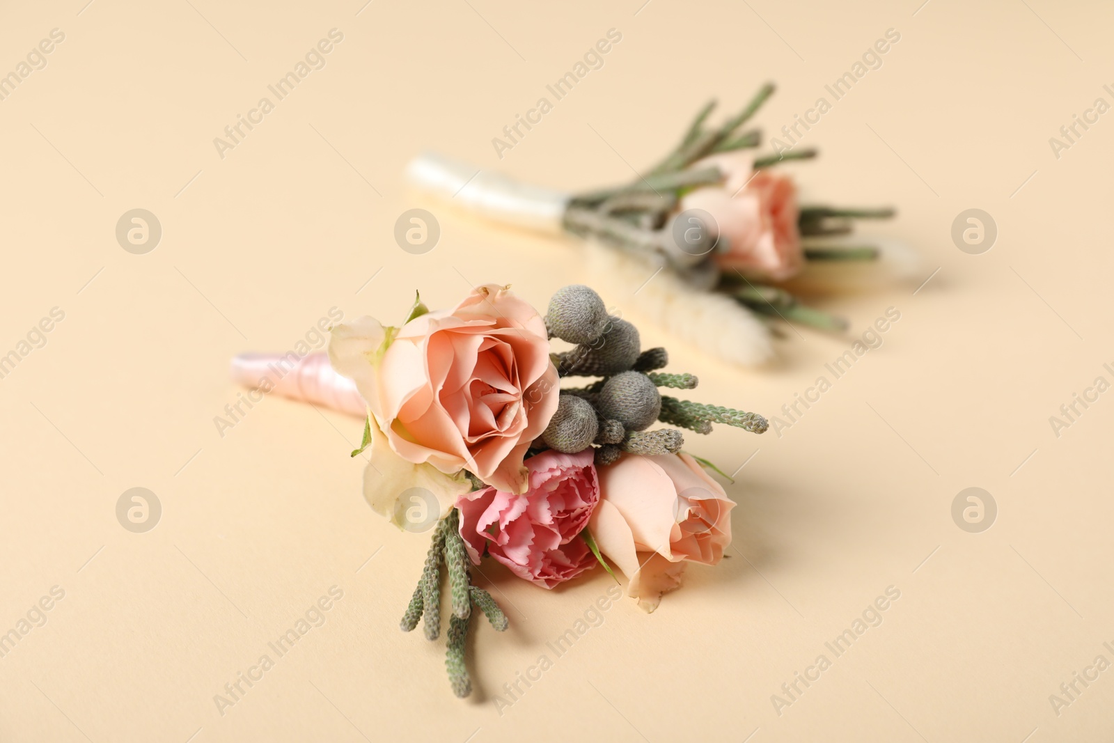 Photo of Boutonnieres with beautiful flowers on beige background, closeup