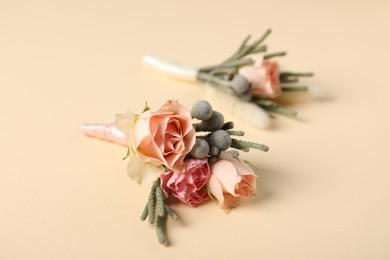 Photo of Boutonnieres with beautiful flowers on beige background, closeup