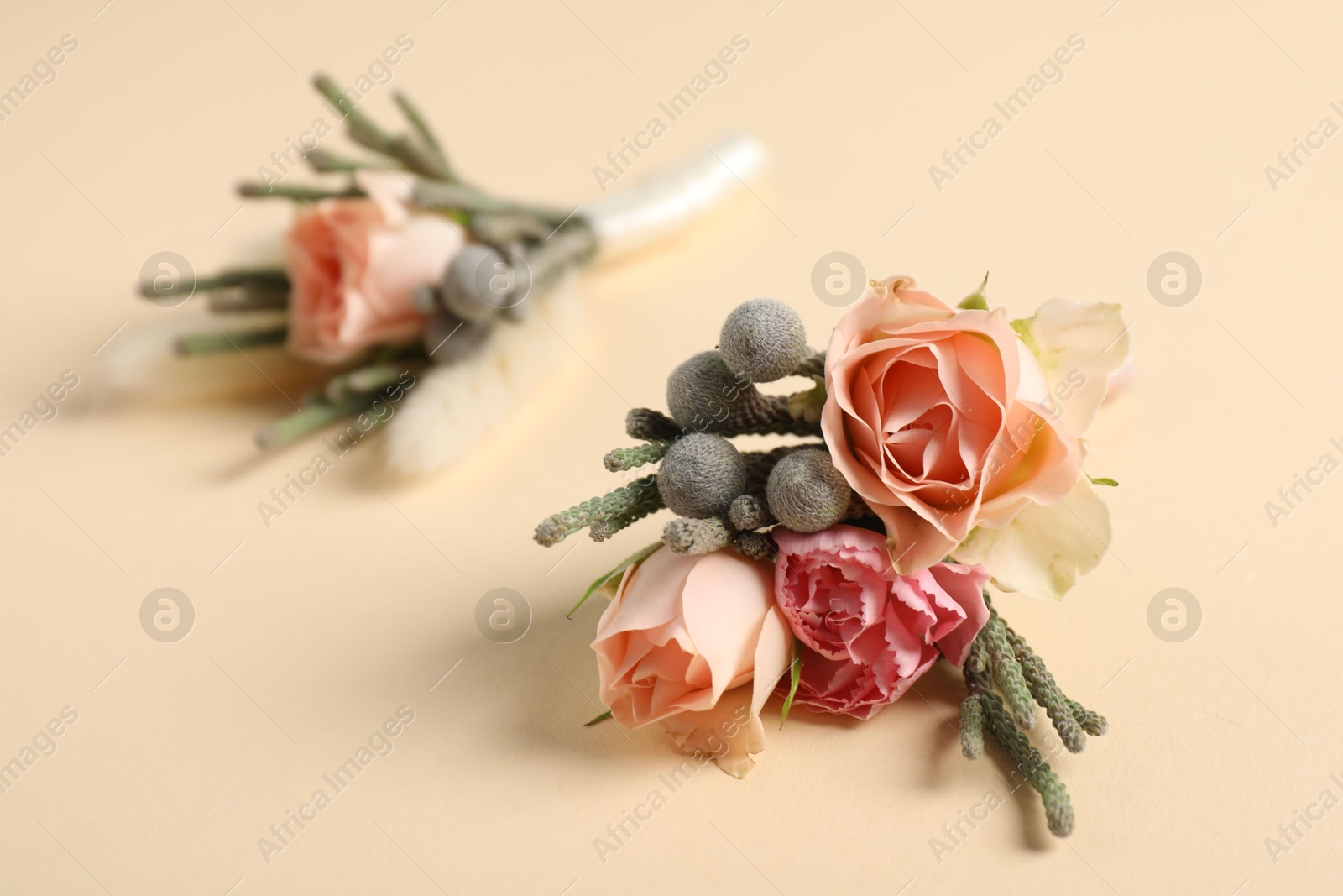 Photo of Boutonnieres with beautiful flowers on beige background, closeup