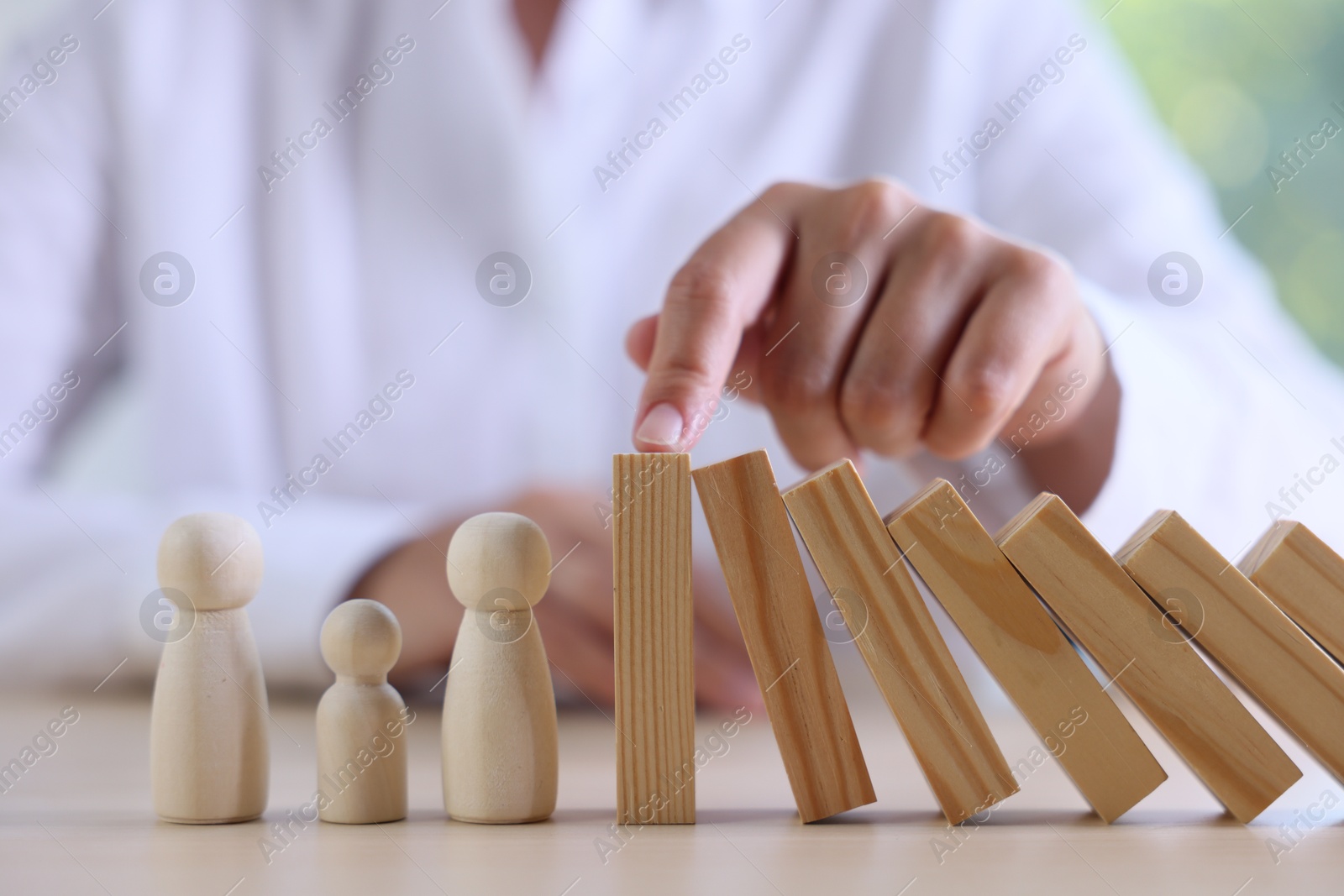 Photo of Risk. Woman stopping domino effect to protect wooden figures at table, closeup