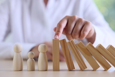 Photo of Risk. Woman stopping domino effect to protect wooden figures at table, closeup