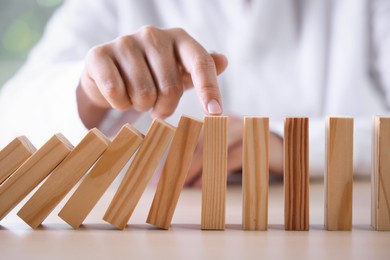 Photo of Risk. Woman stopping domino effect at table, closeup