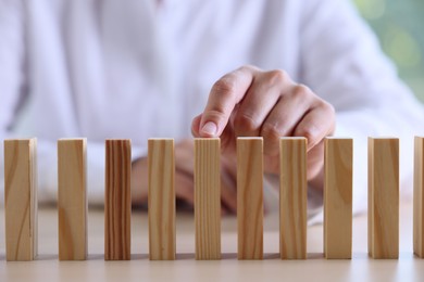 Photo of Risk. Woman pointing at domino tale at table, closeup