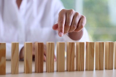 Photo of Risk. Woman pointing at domino tale at table, closeup