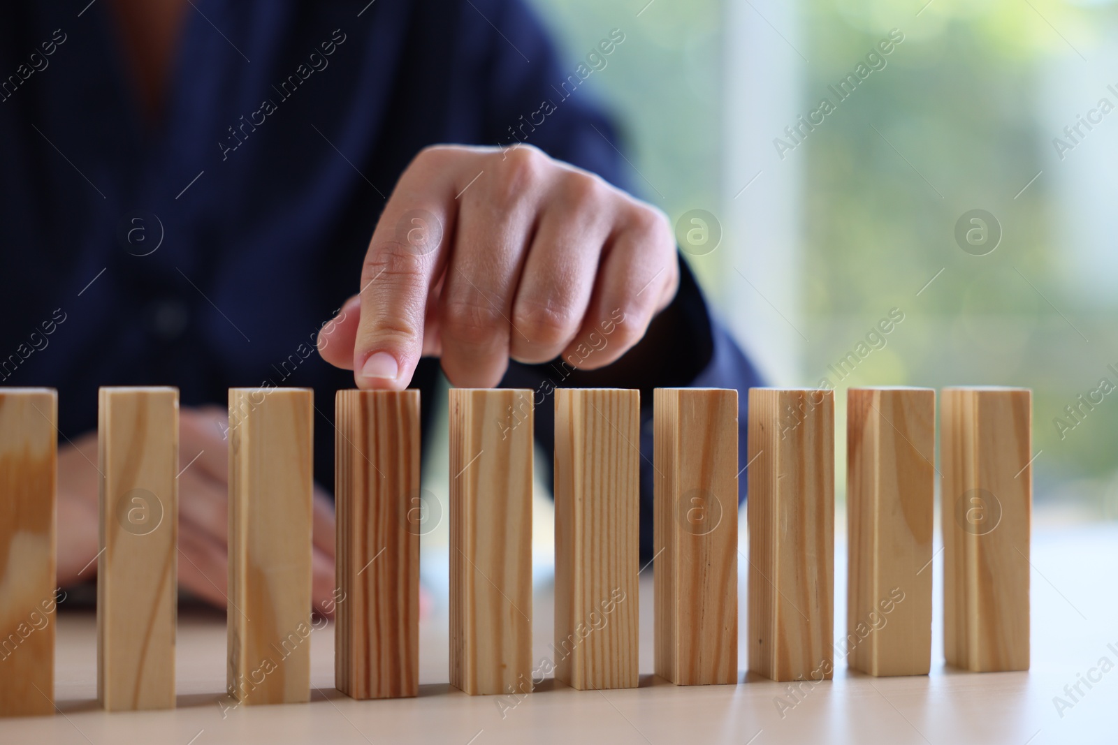 Photo of Risk. Woman pointing at domino tale at table, closeup