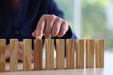 Photo of Risk. Woman pointing at domino tale at table, closeup