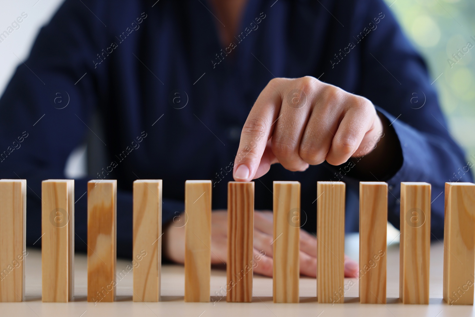 Photo of Risk. Woman pointing at domino tale at table, closeup