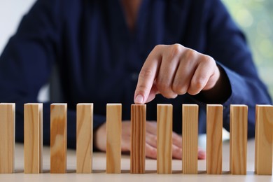 Photo of Risk. Woman pointing at domino tale at table, closeup