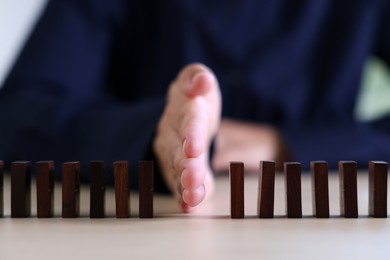 Photo of Risk. Woman stopping domino effect at table, closeup