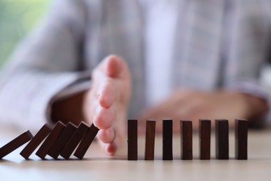 Photo of Risk. Woman stopping domino effect at table, closeup