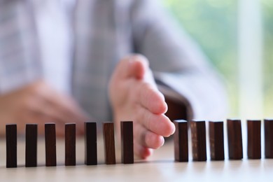 Photo of Risk. Woman stopping domino effect at table, closeup