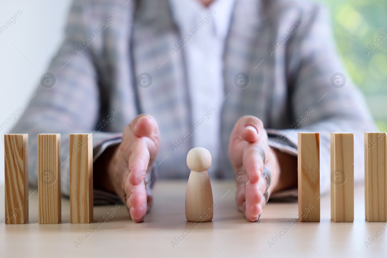 Photo of Risk. Woman stopping domino effect to protect wooden figure at table, closeup