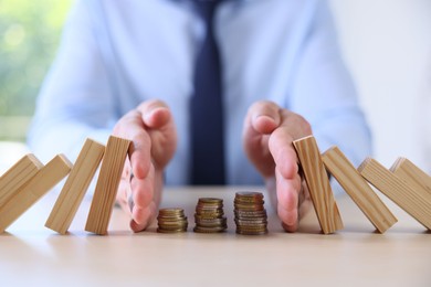 Photo of Risk. Man stopping domino effect to protect coins at table, closeup