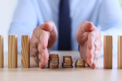 Photo of Risk. Man stopping domino effect to protect coins at table, closeup
