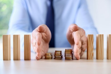 Photo of Risk. Man stopping domino effect to protect coins at table, closeup