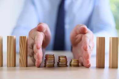 Photo of Risk. Man stopping domino effect to protect coins at table, closeup