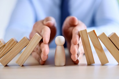 Photo of Risk. Man stopping domino effect to protect wooden figure at table, closeup