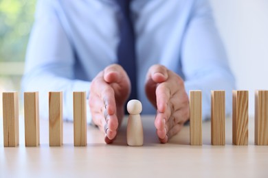 Photo of Risk. Man stopping domino effect to protect wooden figure at table, closeup