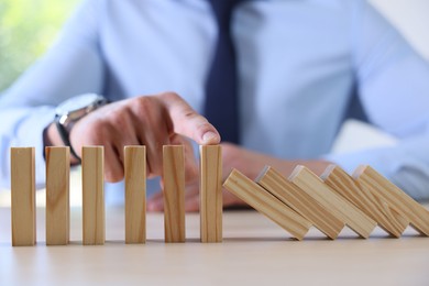 Photo of Risk. Man stopping domino effect at table, closeup