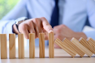 Photo of Risk. Man stopping domino effect at table, closeup