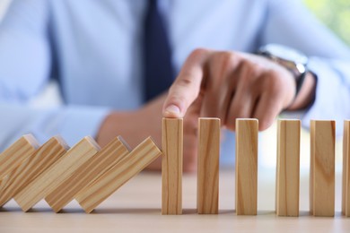 Photo of Risk. Man stopping domino effect at table, closeup