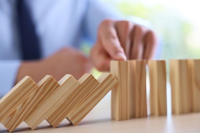 Photo of Risk. Man stopping domino effect at table, closeup