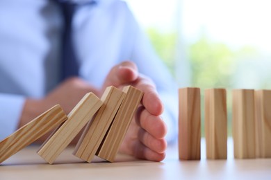 Photo of Risk. Man stopping domino effect at table, closeup