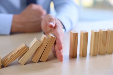 Photo of Risk. Man stopping domino effect at table, closeup