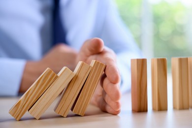 Photo of Risk. Man stopping domino effect at table, closeup