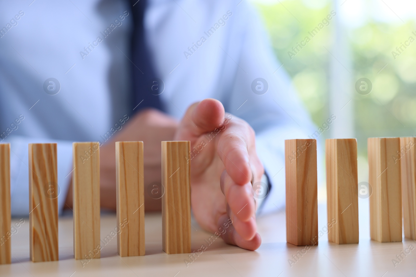 Photo of Risk. Man stopping domino effect at table, closeup