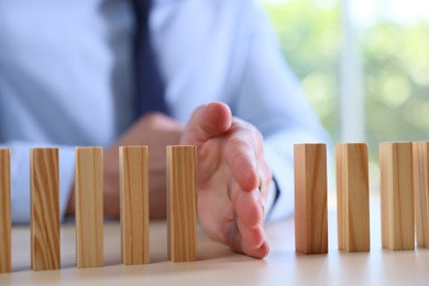 Photo of Risk. Man stopping domino effect at table, closeup
