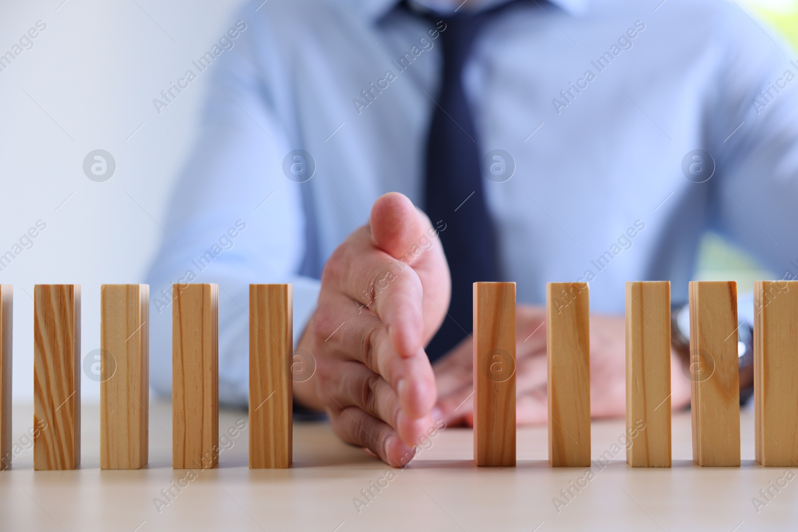 Photo of Risk. Man stopping domino effect at table, closeup