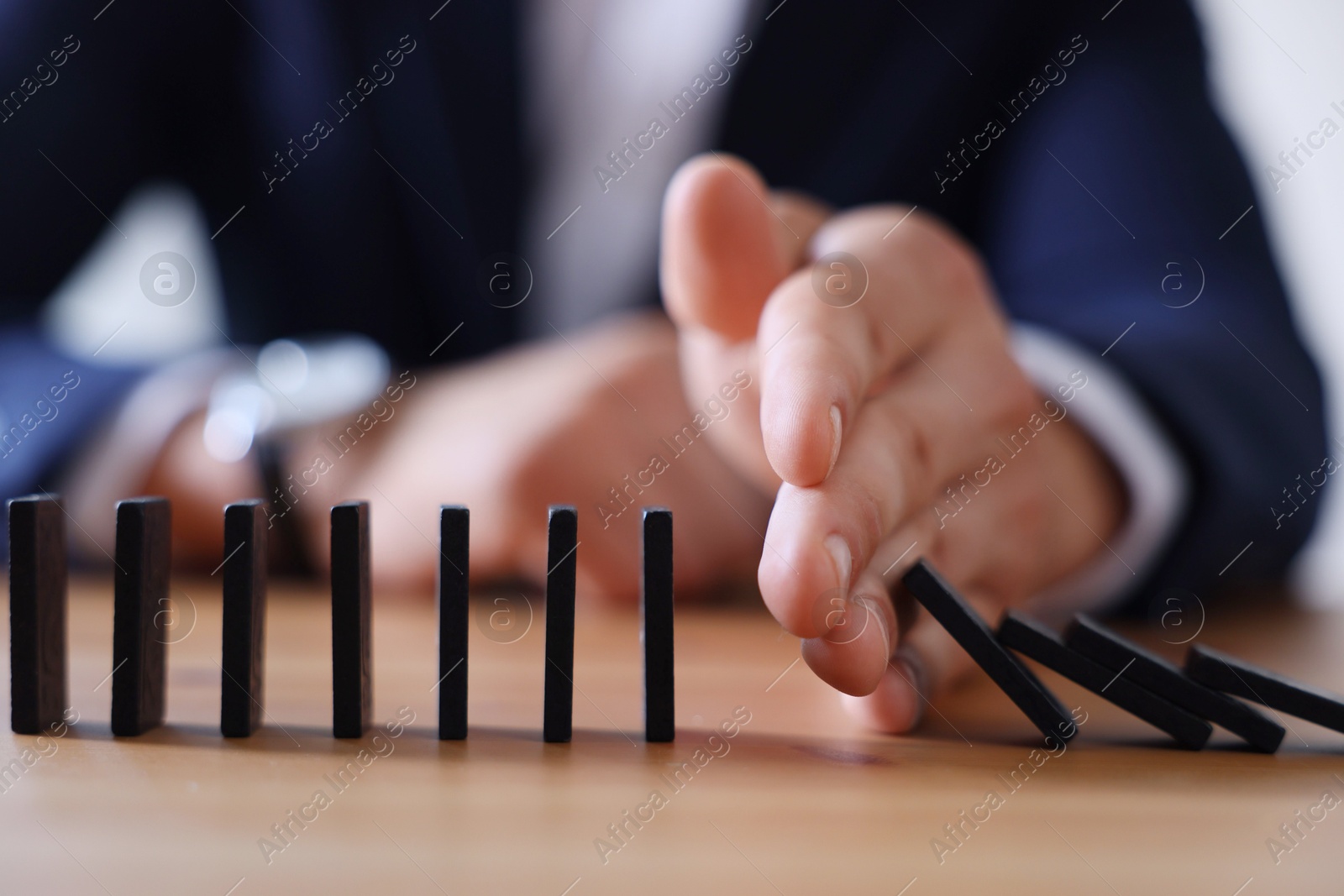 Photo of Risk. Man stopping domino effect at table, closeup